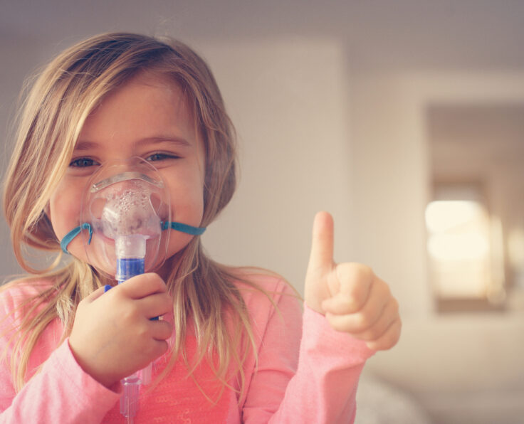 Little girl using inhaler and showing OK. Looking at camera. Space for copy.