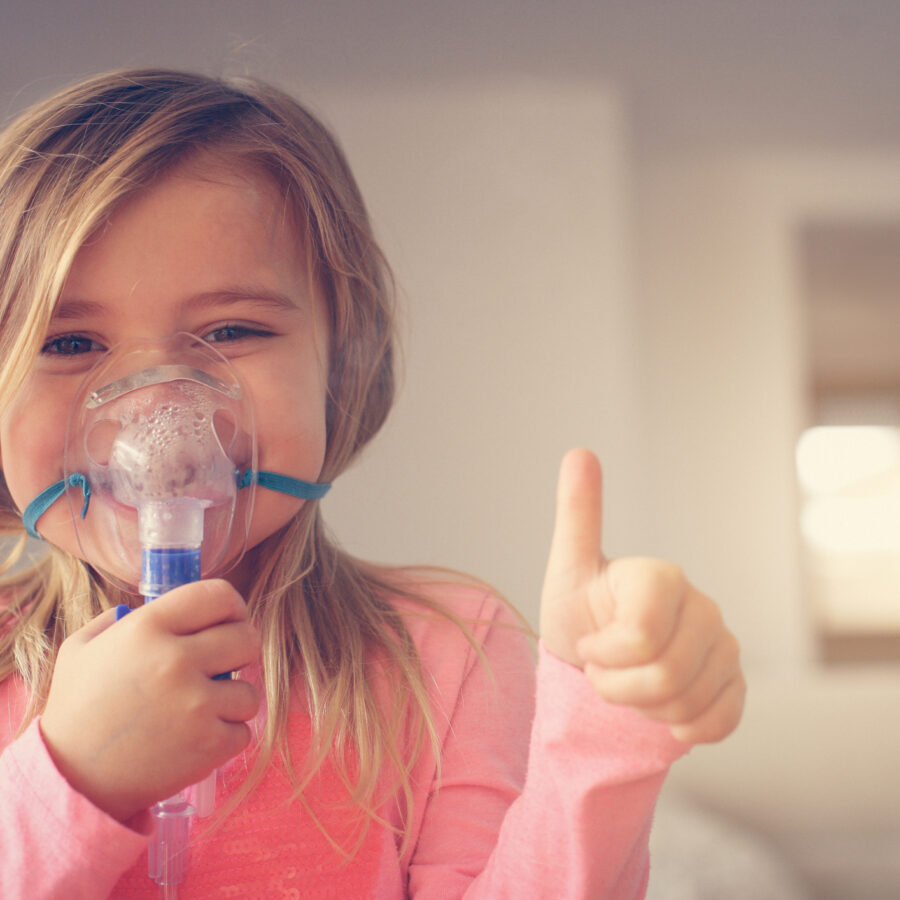 Little girl using inhaler and showing OK. Looking at camera. Space for copy.